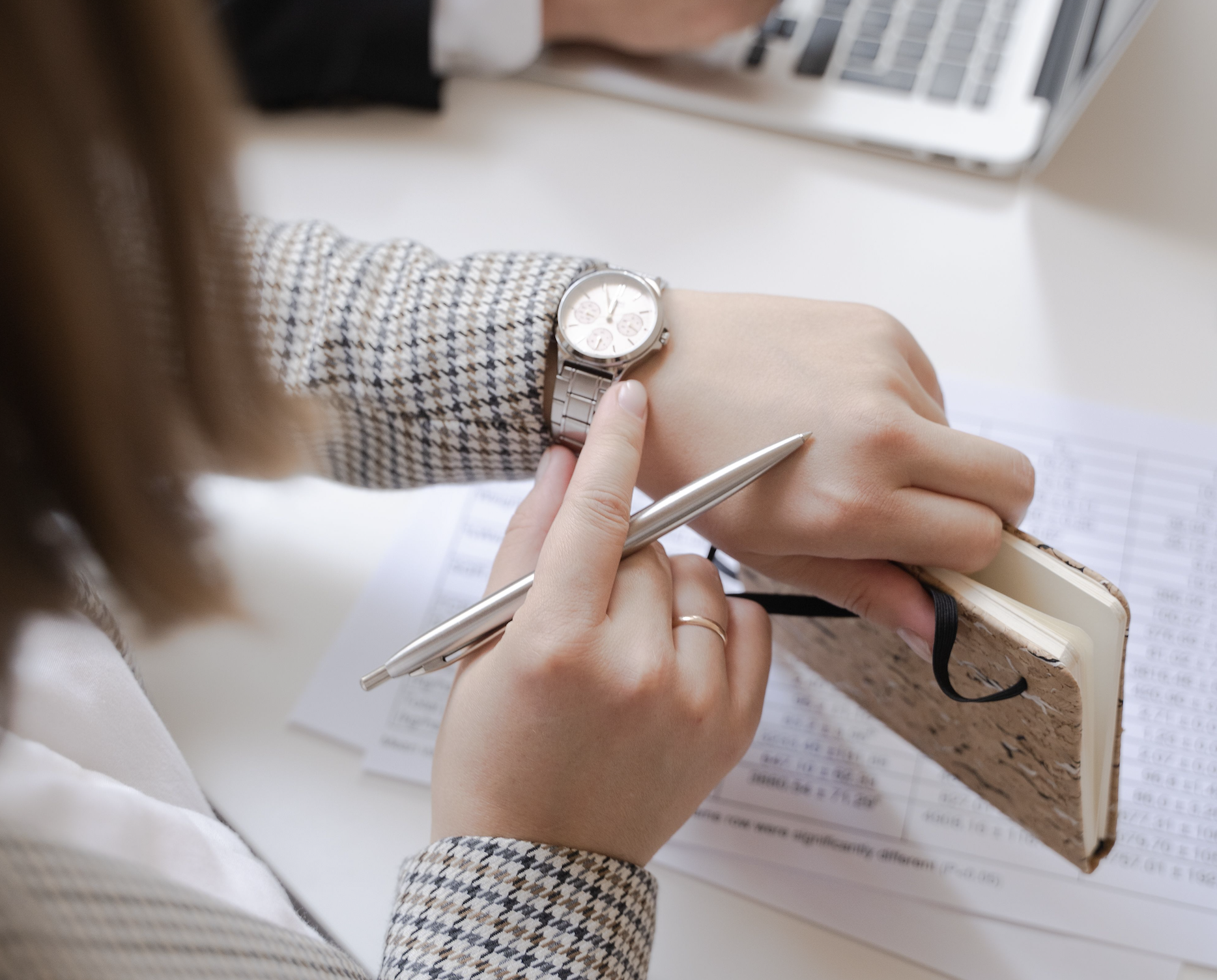 A professional checking the time on a wristwatch while writing notes at a desk